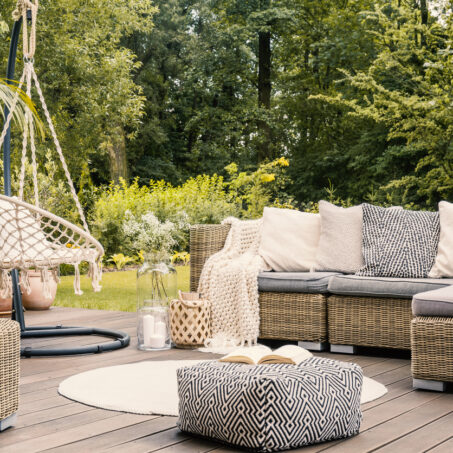 Book on a black and white pouf in the middle of a bright terrace with a rattan corner sofa, hanging chair and round rug. Real photo