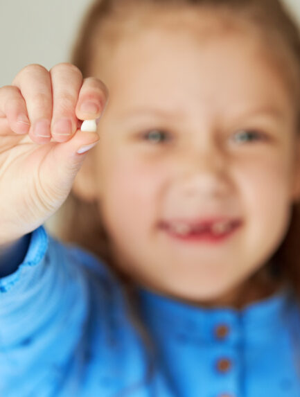 Little girl smiles with her missing tooth in her hand. The concept of pediatric dentistry and dental hygiene