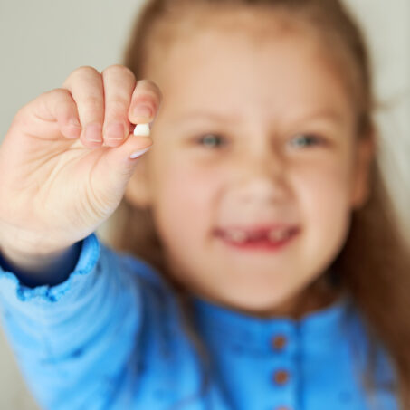 Little girl smiles with her missing tooth in her hand. The concept of pediatric dentistry and dental hygiene