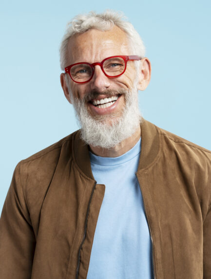 Smiling mature man wearing red hipster glasses looking at camera isolated on blue background