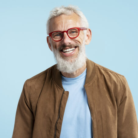Smiling mature man wearing red hipster glasses looking at camera isolated on blue background