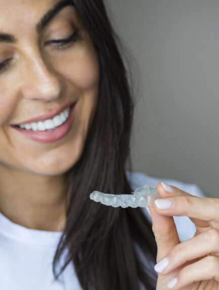 Smiling Woman Holding an Invisible Teeth Aligner