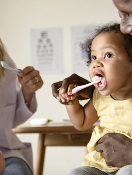 Dentist teaching a little girl how to brush her teeth