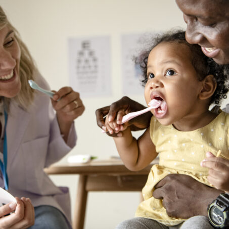 Dentist teaching a little girl how to brush her teeth