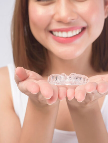 A young smiling woman holding invisalign braces over white background studio, dental healthcare and Orthodontic concept.